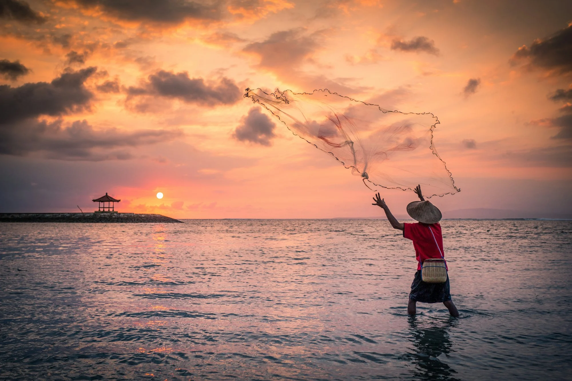 A fisher casting a net at sunset
